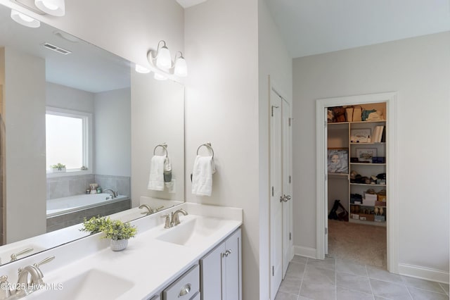 full bath featuring tile patterned flooring, double vanity, baseboards, tiled tub, and a walk in closet
