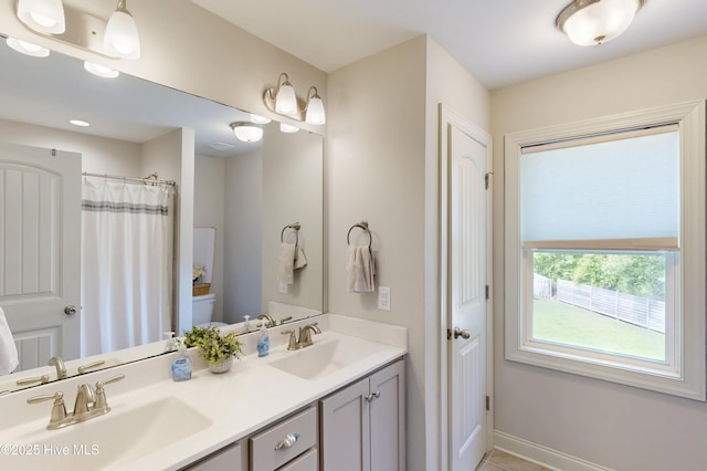 full bath featuring baseboards, double vanity, and toilet