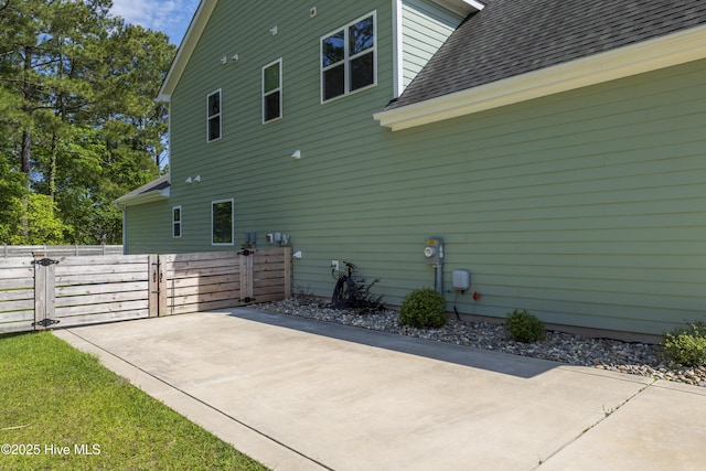 view of side of home featuring a shingled roof, fence, a gate, and a patio area