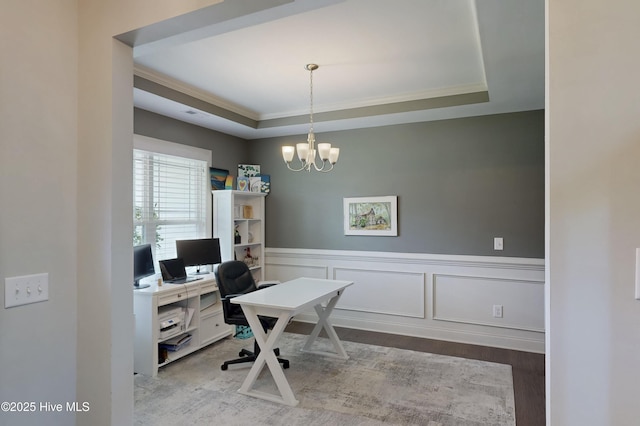 office space with crown molding, wood finished floors, a tray ceiling, a chandelier, and wainscoting