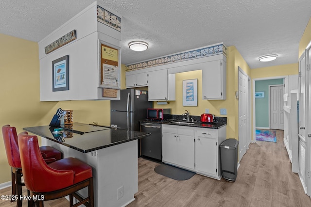 kitchen with appliances with stainless steel finishes, a sink, dark countertops, a peninsula, and light wood-type flooring