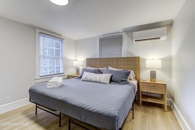 bedroom featuring an AC wall unit, light wood finished floors, baseboards, and crown molding