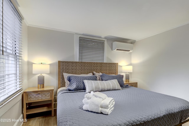 bedroom featuring a wall mounted AC, wood finished floors, crown molding, multiple windows, and baseboards