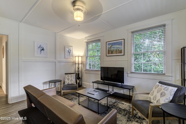 living room with a ceiling fan, wood finished floors, and a decorative wall