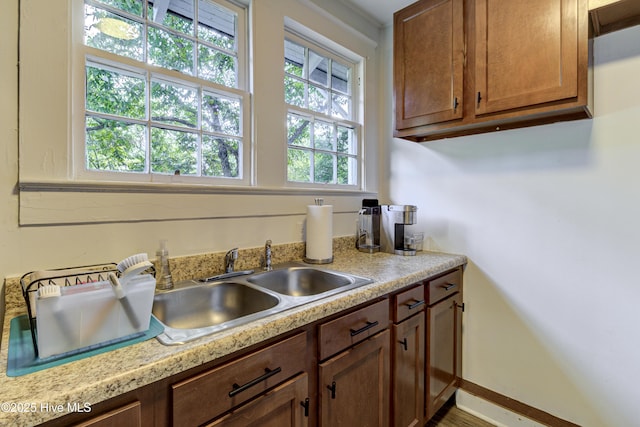 kitchen featuring light countertops, a sink, baseboards, and brown cabinetry
