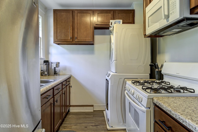 kitchen with white appliances, stacked washer and clothes dryer, light countertops, dark wood finished floors, and baseboards