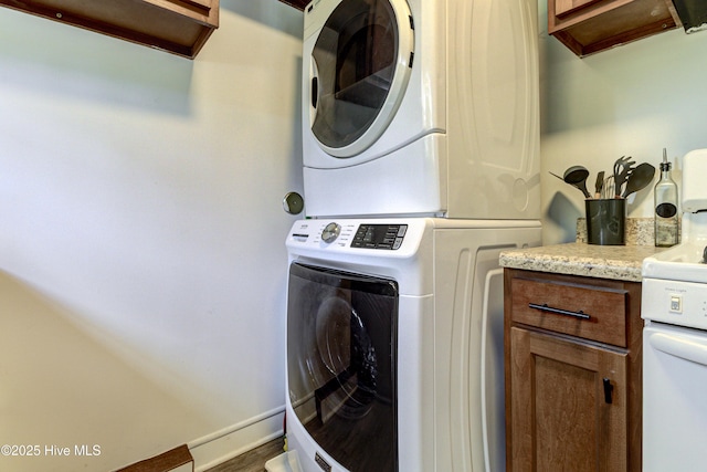 laundry area with stacked washer / dryer, cabinet space, wood finished floors, and baseboards