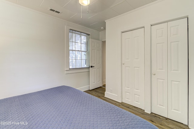 unfurnished bedroom with crown molding, wood finished floors, multiple closets, baseboards, and a ceiling fan