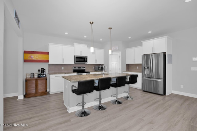kitchen with appliances with stainless steel finishes, a sink, a kitchen breakfast bar, white cabinets, and backsplash