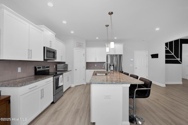 kitchen featuring stainless steel appliances, a sink, a breakfast bar area, light wood-style floors, and recessed lighting