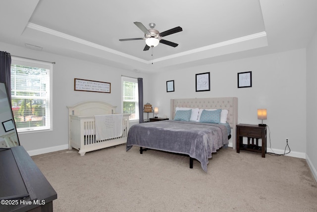 bedroom with a tray ceiling, baseboards, light carpet, crown molding, and ceiling fan