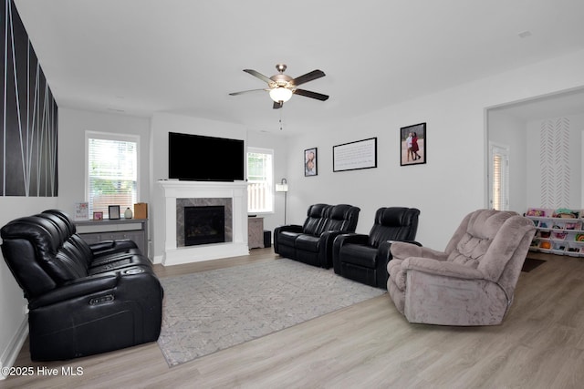 living area featuring healthy amount of natural light, wood finished floors, a ceiling fan, and a fireplace with raised hearth