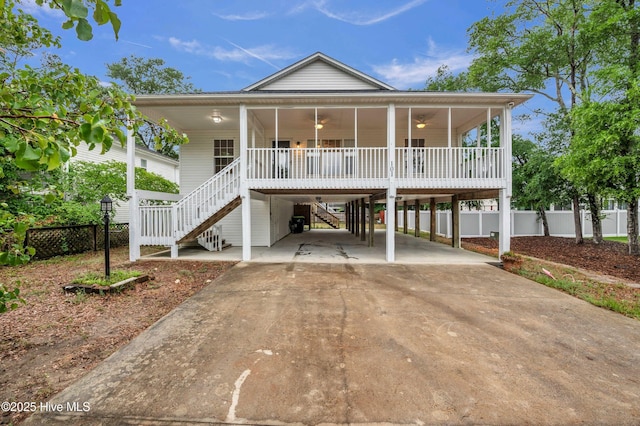 raised beach house featuring concrete driveway, stairway, fence, and a ceiling fan