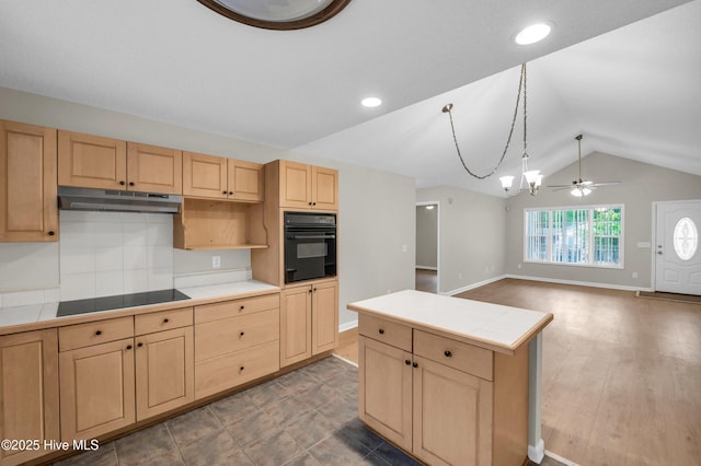 kitchen featuring black appliances, light brown cabinetry, under cabinet range hood, tile countertops, and vaulted ceiling
