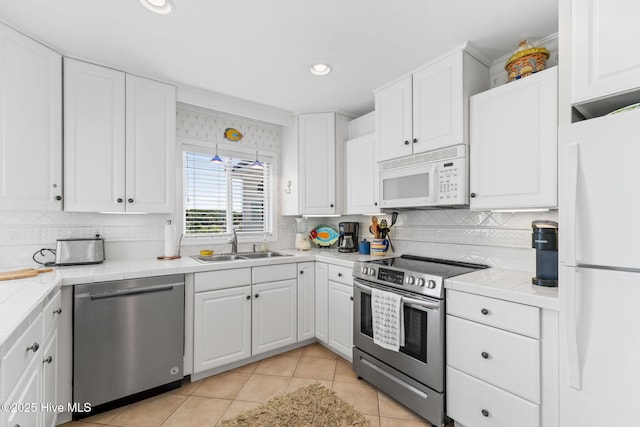 kitchen with stainless steel appliances, a sink, tile countertops, white cabinetry, and recessed lighting
