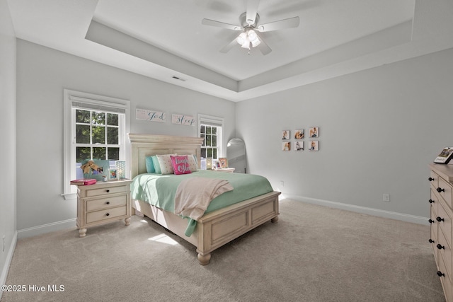 bedroom featuring light colored carpet, a raised ceiling, baseboards, and multiple windows