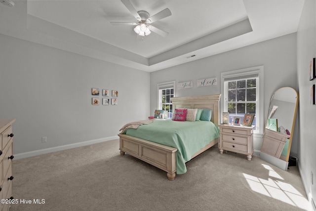 bedroom with light colored carpet, multiple windows, a raised ceiling, and baseboards