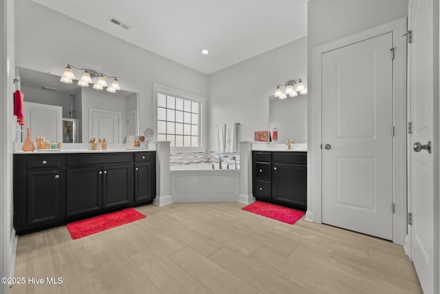 bathroom featuring two vanities, a garden tub, wood finished floors, and recessed lighting