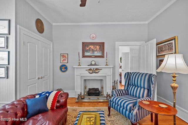 living area with wood finished floors, crown molding, a ceiling fan, a fireplace, and baseboards