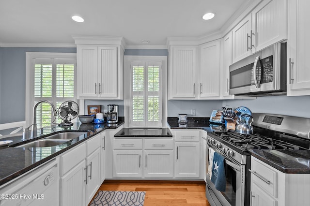 kitchen with stainless steel appliances, a sink, white cabinets, crown molding, and light wood-style flooring