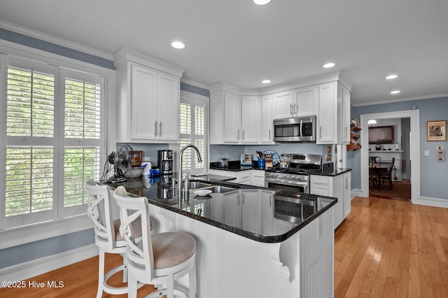 kitchen with appliances with stainless steel finishes, a sink, white cabinetry, plenty of natural light, and ornamental molding