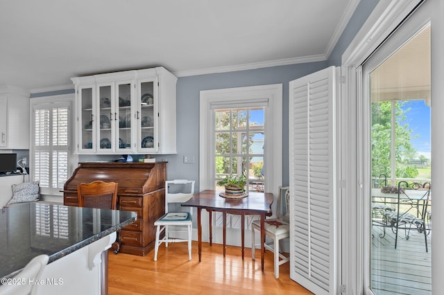 kitchen with light wood finished floors, white cabinetry, glass insert cabinets, dark stone counters, and ornamental molding