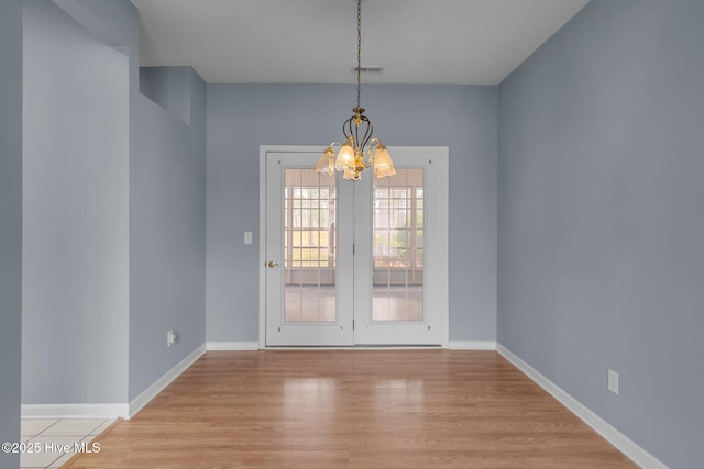 unfurnished dining area featuring a chandelier, light wood-style flooring, and baseboards