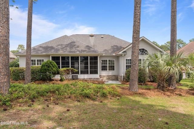 back of property with a sunroom, roof with shingles, and a yard
