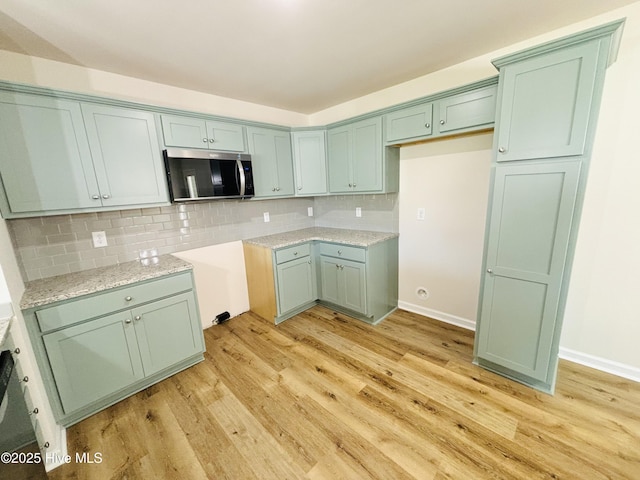 kitchen with stainless steel microwave, light wood-type flooring, backsplash, and light stone counters