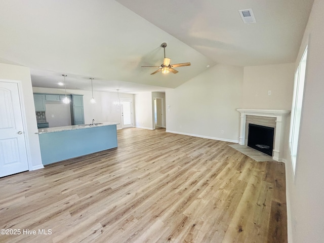 unfurnished living room with ceiling fan, light wood-style floors, vaulted ceiling, a fireplace with flush hearth, and baseboards