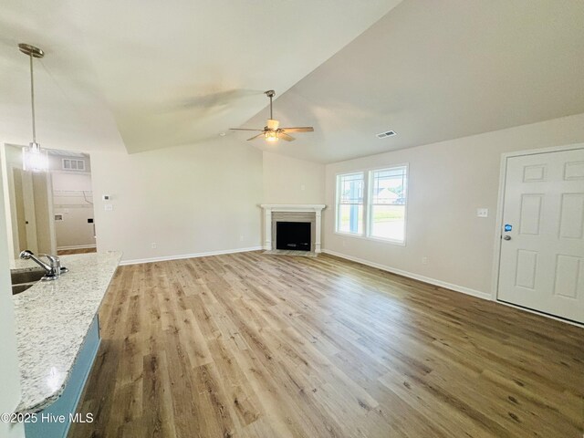 unfurnished living room featuring ceiling fan, a sink, baseboards, wood finished floors, and a fireplace with flush hearth