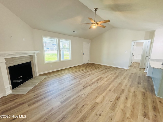 unfurnished living room featuring ceiling fan, vaulted ceiling, light wood-style floors, a fireplace with flush hearth, and baseboards