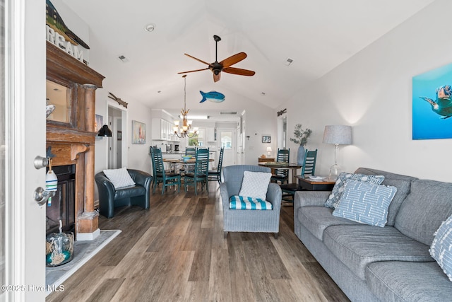living area with dark wood-style floors, a ceiling fan, a fireplace with raised hearth, lofted ceiling, and a chandelier