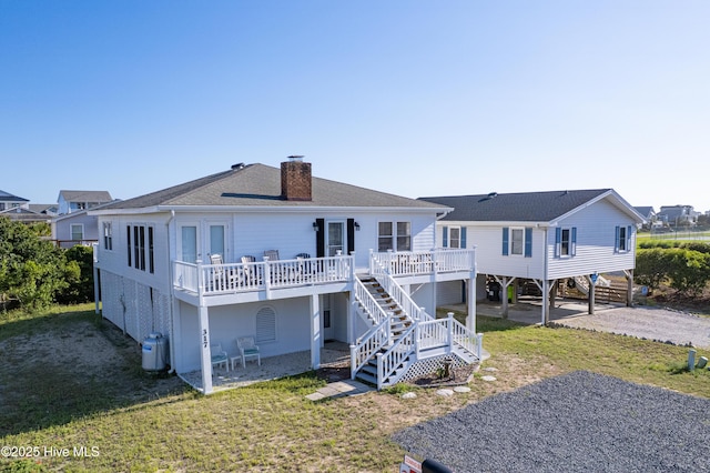 rear view of property featuring dirt driveway, a chimney, stairs, a deck, and a yard