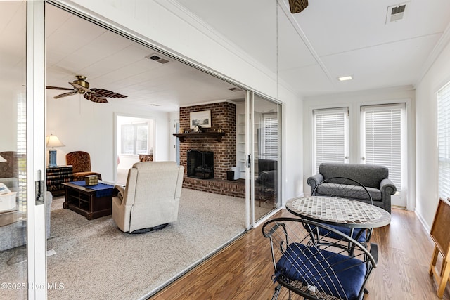 living room featuring a fireplace, wood finished floors, ornamental molding, and a ceiling fan