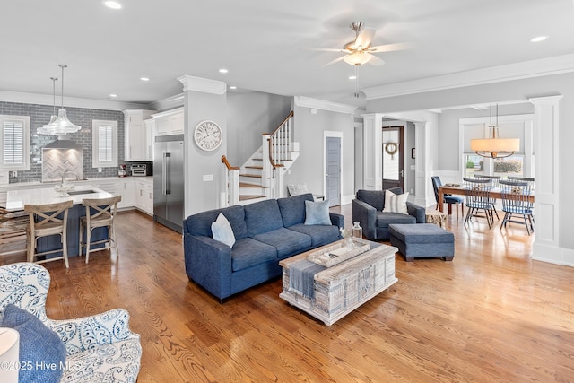 212 Cornubia Dr, Castle Hayne, NC 28429 - living area featuring light wood finished floors, ceiling fan, ornamental molding, stairway, and decorative columns