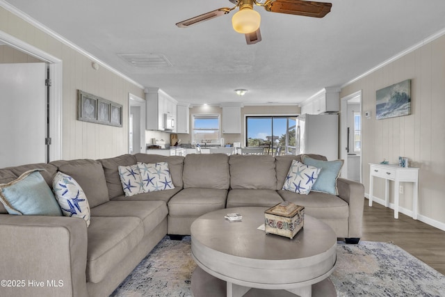 living room with ornamental molding, a ceiling fan, wood finished floors, baseboards, and wood walls