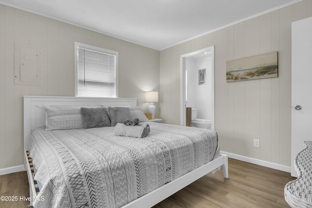 bedroom featuring ornamental molding, wood finished floors, baseboards, and ensuite bath