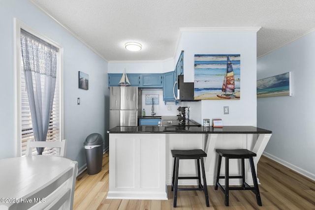 kitchen featuring a peninsula, blue cabinets, light wood-style flooring, ornamental molding, and appliances with stainless steel finishes