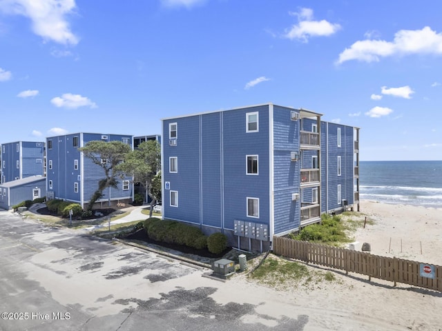 view of building exterior featuring view of water and beach and fence
