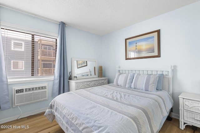 bedroom featuring light wood finished floors, a wall mounted AC, a textured ceiling, and baseboards