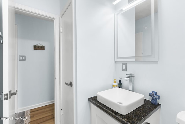 half bath featuring wood finished floors, vanity, and baseboards