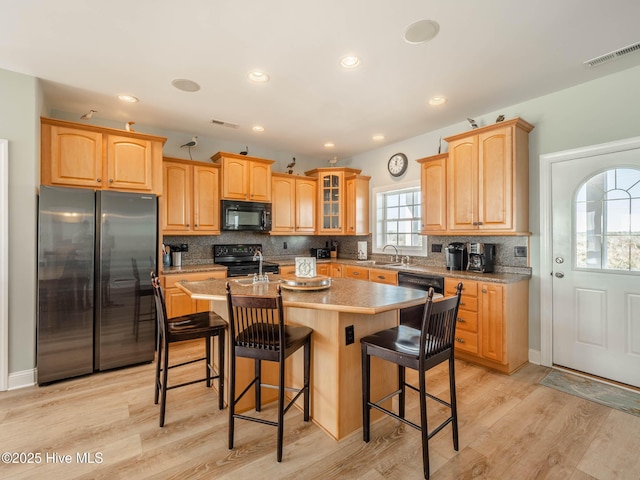 4388 Island Dr, North Topsail Beach, NC 28460 - kitchen featuring black appliances, a kitchen island with sink, tasteful backsplash, light wood-style flooring, and a breakfast bar