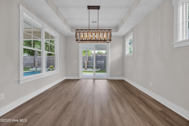 unfurnished dining area featuring wood finished floors, a chandelier, baseboards, and a tray ceiling