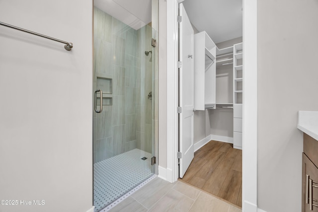 full bath with a stall shower, a spacious closet, vanity, and baseboards