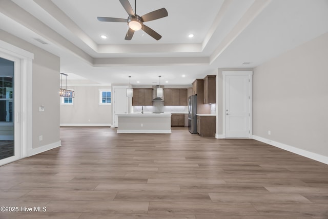 unfurnished living room featuring ceiling fan, a raised ceiling, wood finished floors, and recessed lighting