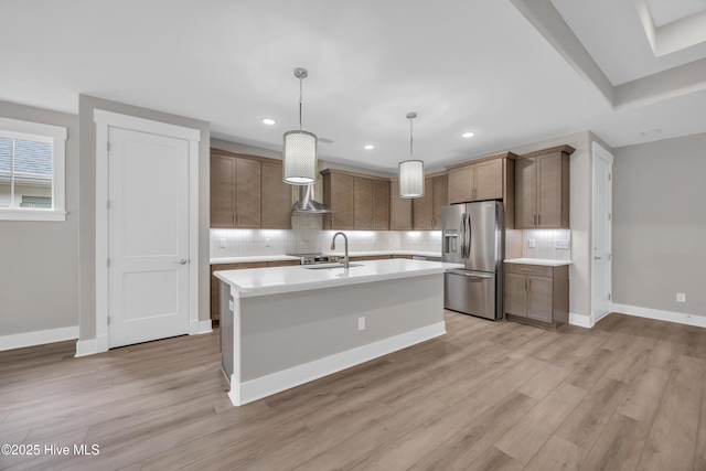 kitchen with stainless steel fridge, light countertops, a sink, decorative backsplash, and light wood-style flooring