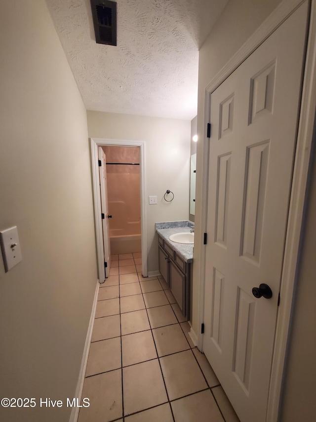 full bath featuring tile patterned floors, vanity, a textured ceiling, baseboards, and a tub to relax in