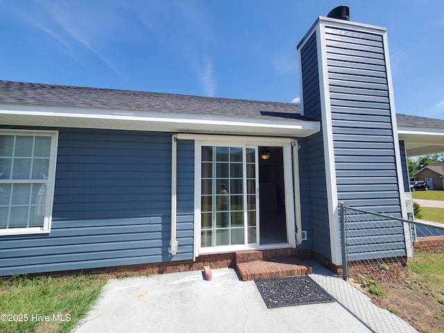 entrance to property featuring a chimney and a shingled roof