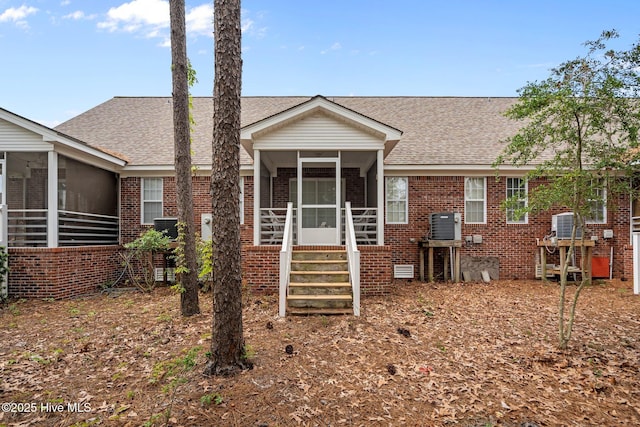 rear view of property featuring a sunroom, brick siding, and roof with shingles